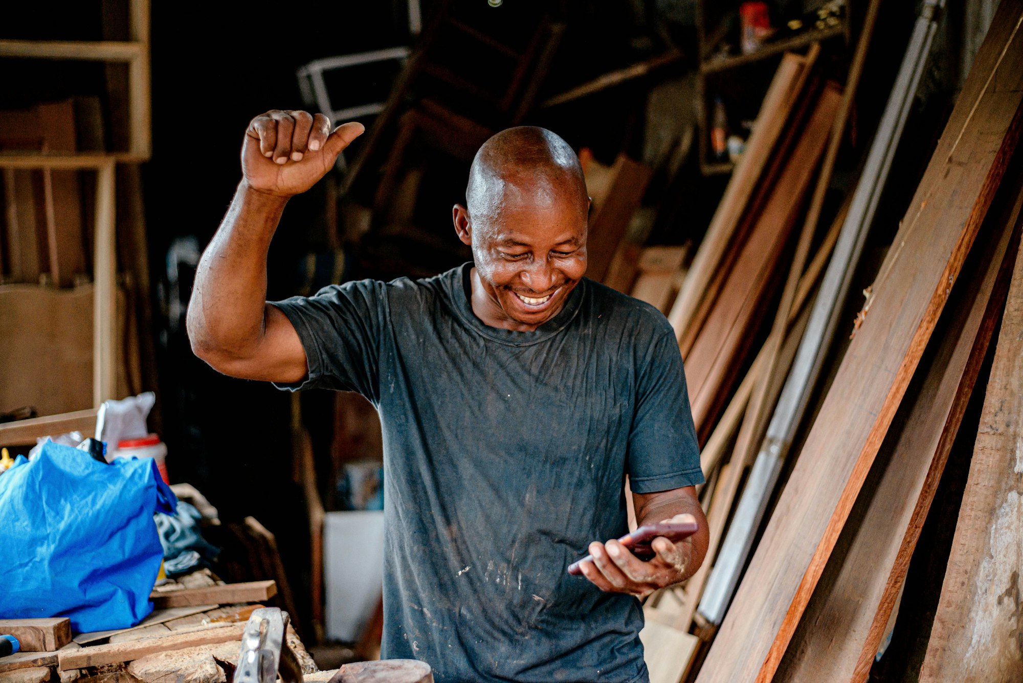 A carpenter smiling at his phone in his workshop